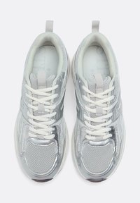 Scarpe da ginnastica argento con tomaia in mesh textured, dettagli riflettenti, lacci bianchi spessi e colletto imbottito. Suola in gomma con leggera scolpitura.