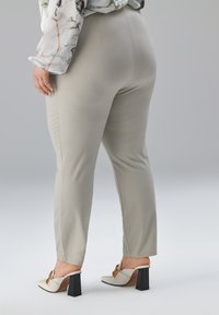 Lichtgrijze, nauwsluitende broek met een gladde textuur, voorzien van een hoge taille en zijnaden. Gecombineerd met witte hakken en gouden accenten.