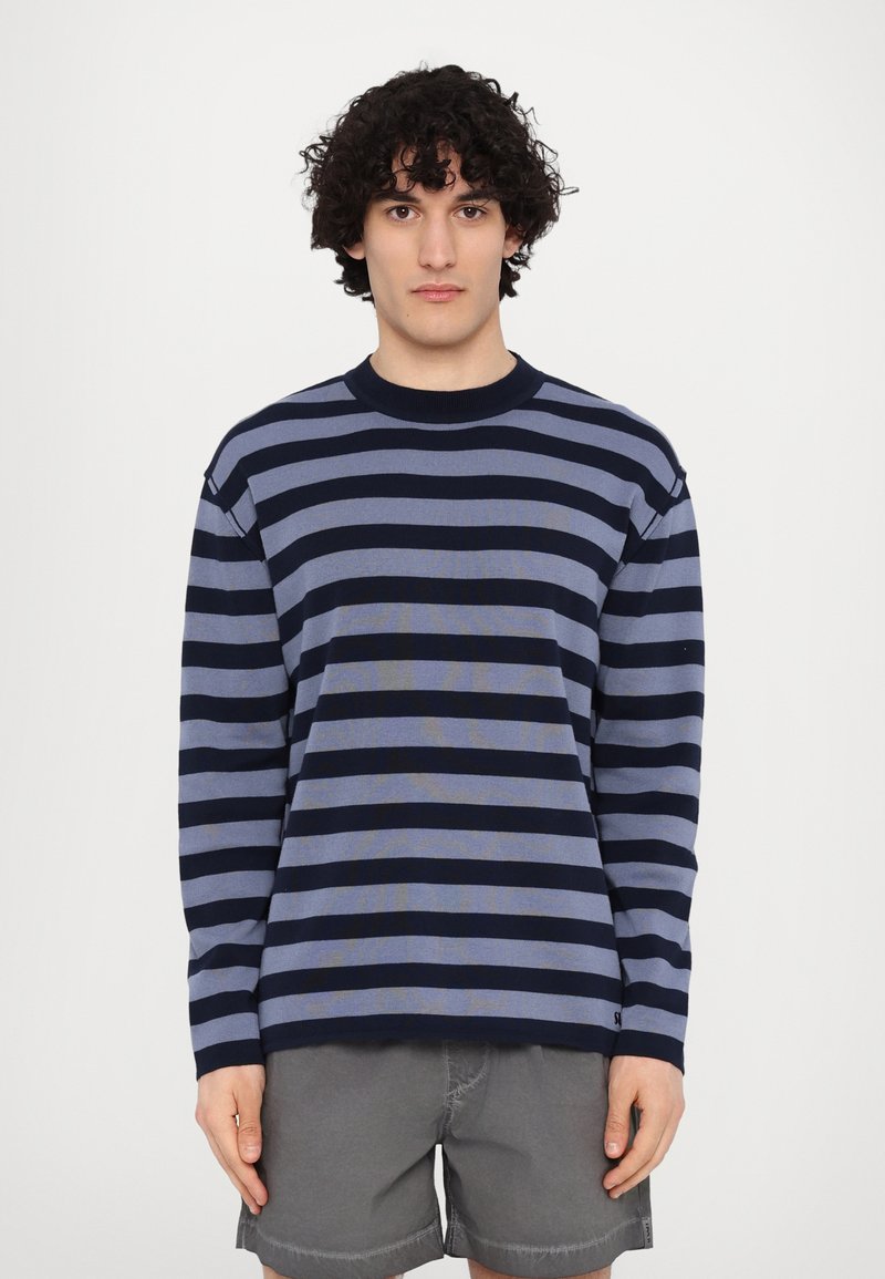 Navy and light blue striped long-sleeve sweater with a crew neckline and ribbed cuffs, paired with gray shorts. Textured fabric.
