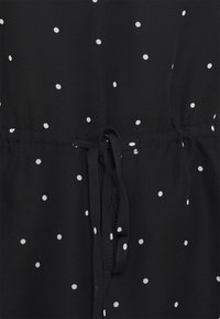 Robe en tissu noir à pois blancs, avec une taille élastique et un détail de nœud. Texture douce avec une coupe décontractée.