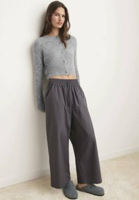 Grijze cropped cardigan met knopen, gecombineerd met donkergrijze wijde broek en grijze instappers. Zachte texturen, casual pasvorm, minimalistisch ontwerp.