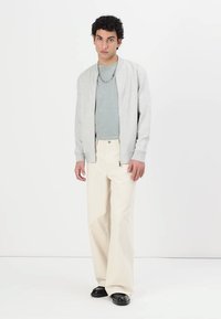 Light gray bomber jacket over a teal shirt, paired with cream wide-leg pants. The look features minimalistic design and a relaxed fit.