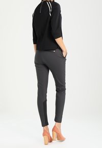 Svart topp med vita randiga detaljer och dragkedja, tillsammans med mörkgrå tajta byxor med sidoficka. Modellen bär ljusrosa klackar.