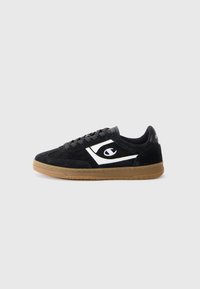 Black suede sneaker with a white logo, rubber gum sole, and black laces. Features a low-top design and smooth texture.