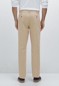 Beige trousers made of smooth fabric with two back pockets, featuring button closures and a straight-leg cut. Worn with dark footwear.