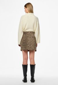 Kremfarget strikket genser med høy hals, kombinert med et mini skjørt i leopardmønster. Svarte knelange støvler fullfører antrekket.
