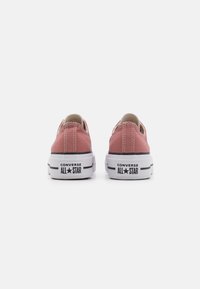 Baskets en toile rose avec semelles en caoutchouc blanches, coutures contrastées et logo noir "CONVERSE ALL STAR" sur le talon. Design basses.