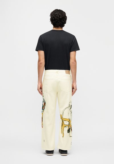 Ευρύχωρα, κρεμ παντελόνια με καλλιτεχνικές εικονογραφήσεις σε κάθε πόδι, σε συνδυασμό με μια μ αύρη κοντομάνικη μπλούζα. Παπούτσια με λαστιχένια σόλα συμπληρώνουν την εμφάνιση.