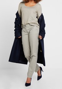 Lichtbeige langwerpige top, grijze tapse broek met zijzakken, en marineblauwe jas met een kraag, gecombineerd met donkerblauwe hoge hakken.