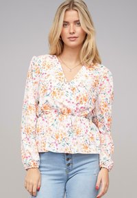 Blusa floreale con scollatura a V, maniche lunghe e vita arricciata. Presenta piccoli motivi rosa, arancioni e verdi su uno sfondo bianco.