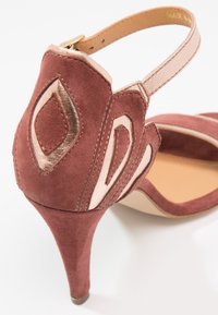 Sandale à talon haut en daim marron avec des accents décoratifs métalliques en or rose et crème, et une bride de cheville avec fermeture à boucle.