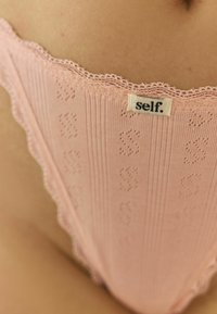 Roosa pitsilised stringid, millel on ribakujuline tekstuur, sisaldades peent mustrit ja vööl silti "self.".
