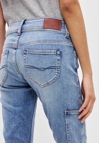 Ανοικτού μπλε τζιν παντελόνι με δερμάτινο τμήμα που φέρει την ετικέτα "Pepe Jeans." Διαθέτει διπλές πίσω τσέπες και αντίθετο ραφάρισμα.