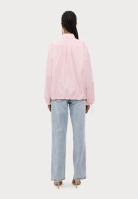 Camisa oversized às riscas em rosa e branco com punhos e bainha elásticos, combinada com jeans largos em azul claro desbotado e saltos em bege.