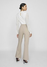 Blusa blanca texturizada con mangas largas y espalda con apertura en forma de llave, combinada con pantalones beige de cintura alta y sandalias negras de tacón alto.