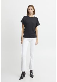 Svart kortärmad t-shirt med rund halsringning, i kombination med vita utsvängda jeans och svarta anklarstövlar med vita accenter.