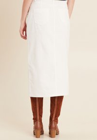 Jupe midi en denim blanc au design droit, avec deux poches arrière et un ourlet subtil. Associée à des bottes en suède marron mi-mollet.