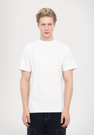 T-shirt en coton blanc avec un col rond et des manches courtes, présentant une coupe décontractée et une texture lisse, associé à un pantalon bleu foncé.
