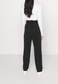 Zwarte, brede broek met een geplooide elastische tailleband en zijzakken, gecombineerd met witte sneakers. Gladde textuur en relaxte pasvorm.