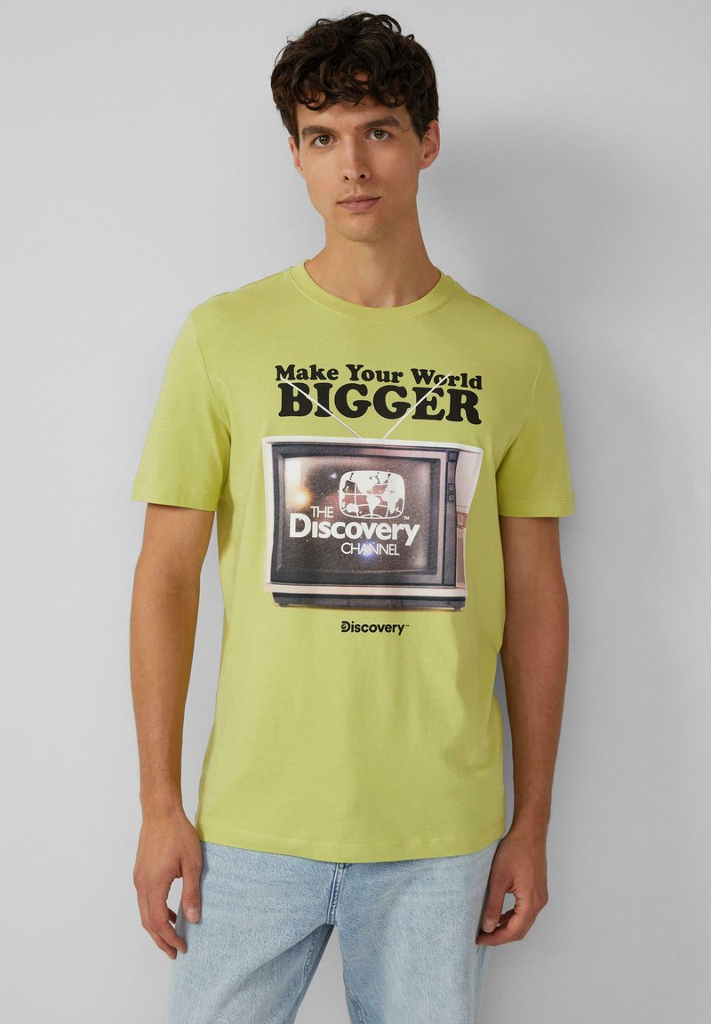 Limoengroene katoenen t-shirt met een afbeelding van een oude televisie met de tekst "Maak je wereld GROTER" en het logo van "The Discovery Channel".