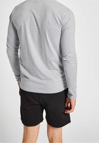 Maglietta a maniche lunghe grigia in tessuto morbido, abbinata a pantaloni corti neri. Cuciture visibili e design aderente, con orlo arrotondato nella parte inferiore.