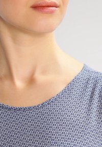 Modrá látka s potiskem a malými bílými květinovými vzory, s kulatým výstřihem a hladkou texturou, viděná od ramene nahoru.