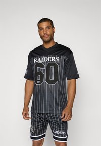 Juodas tinklinis sportinis marškinėliai su vertikaliomis baltomis juostelėmis, priekyje yra užrašai "RAIDERS" ir "60". Tai derinama su atitinkančiomis šortais, papuoštomis logotipu ir juostelėmis.