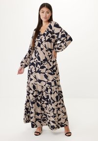 Maxi šaty z béžové látky s abstraktním námořnickým vzorem, výstřih do V, dlouhými rukávy, vrstveným designem a nařaseným pasem. Černé otevřené lodičky.