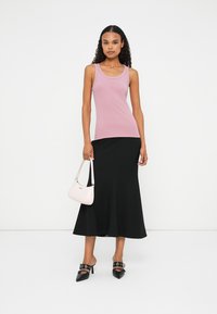 Roze tanktop, zwarte midi-rok en zwarte hakken. Accessoire: kleine roze handtas. Gladde texturen en aansluitende silhouet.