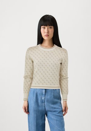 Vaaleanbeige neule, jossa on timanttikuosi, ribbaus kaula-aukossa ja hihansuissa, slim fit -malli, käytössä löysien sinisten housujen kanssa. Suunnikas rakenne.