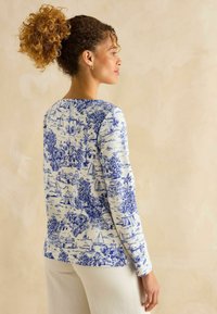 Langärmliges Oberteil in Weiß mit blauem Landschaftsdruck, der Palmen, Segelboote und Häuser zeigt. Weicher Stoff mit Rundhalsausschnitt und geradem Schnitt.