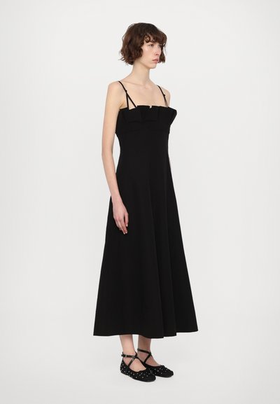 Rochie neagră fără mâneci, cu un corset ajustat și o fustă evazată. Are bretele subțiri și un accent pliat la decolteu. Textură netedă.