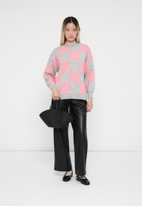 Grijs en roze geruite trui met een oversized pasvorm, gecombineerd met zwarte leren wijde broek en een zwarte handtas.