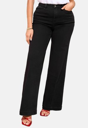 Schwarze Denim-Hosen mit weitem Bein, hoher Taille, oberem Knopf und Taschen. Kombiniert mit roten Sandalen mit Riemchen und einem weißen T-Shirt.