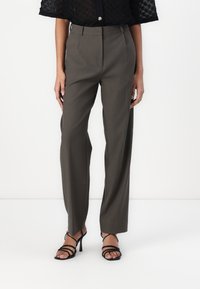 Pantalons taille haute, ample, en tissu vert olive, avec des plis frontaux et un design à jambe droite. Associés à des talons aiguilles noirs à lanières.