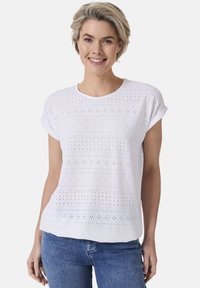 Weißes Baumwolloberteil mit Lochstickerei und Broderiemuster, rundem Ausschnitt und kurzen, aufgerollten Ärmeln. Kombiniert mit Denim-Unterteilen.