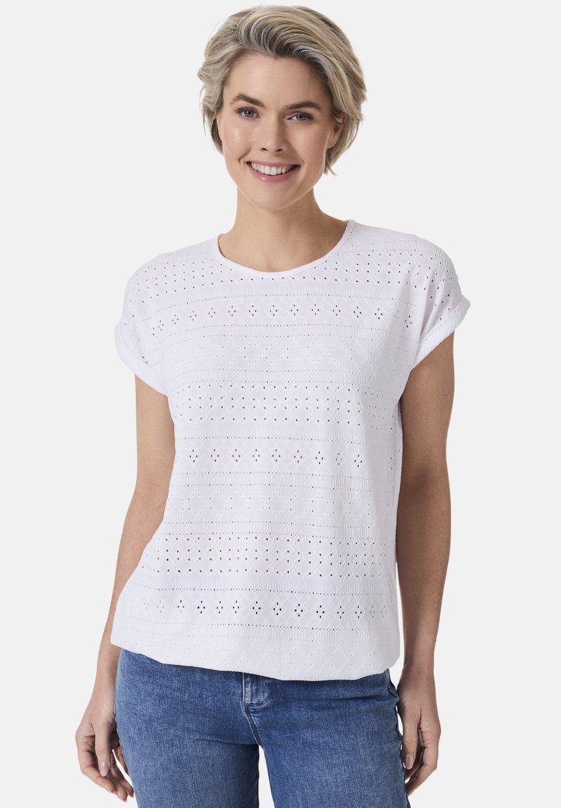 Weißes Baumwolloberteil mit Lochstickerei und Broderiemuster, rundem Ausschnitt und kurzen, aufgerollten Ärmeln. Kombiniert mit Denim-Unterteilen.