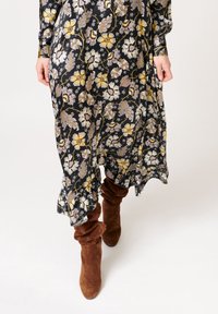 Dlouhé černé šaty s květinovým vzorem v žluté, fialové a bílé barvě; volánkový lem a dlouhé rukávy, doplněné hnědými pohodlnými kozačkami do kolen.