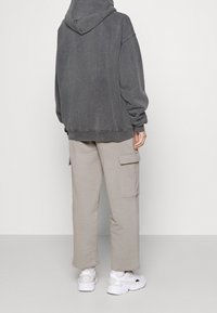 Felpa grigia con cappuccio e vestibilità relaxed, abbinata a pantaloni cargo beige chiaro con tasche laterali. Indossata con sneakers sportive bianche.