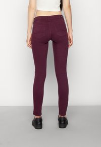 Burgundy smala byxor i bomull med en slät yta. Modellen visar baksidan som har två bakfickor och en bältesöppning.