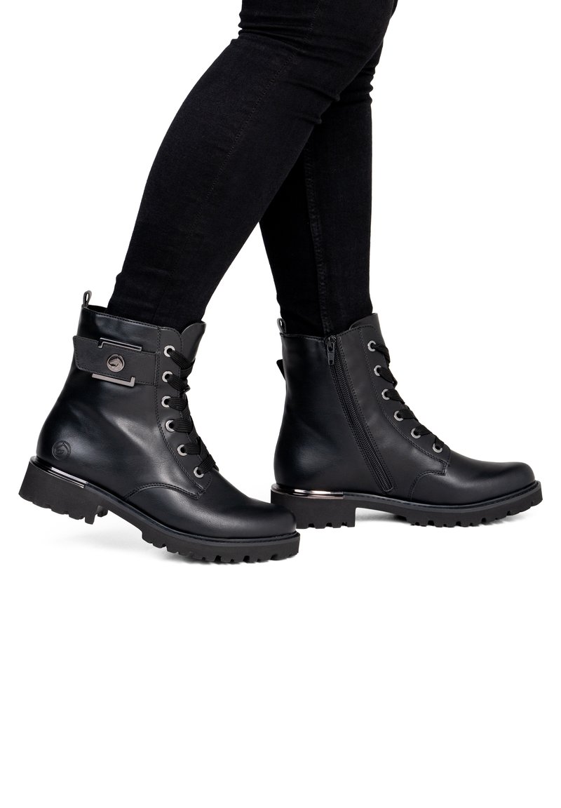 Bottines en cuir noir à lacets et fermeture éclair latérale portées avec un pantalon slim noir sur fond blanc.