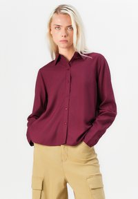 Burgundy button-up shirt with a collar, long sleeves, and a relaxed fit, paired with beige cargo pants featuring side pockets.