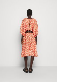 Kukkamekko puff-hihnoilla, oranssia ja valkoista kuosia, puolipitkä hame röyhelöhelmalla, takana sidottu yksityiskohta ja rento malli.