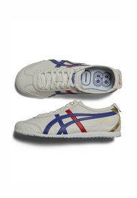 Sneakers in pelle bianca con accenti blu e rossi, caratterizzati da una suola testurizzata, strisce distintive e dettagli dorati sul retro.