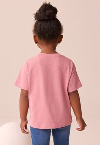 T-shirt en coton rose à manches courtes, coupe décontractée et encolure arrondie, associé à un jean en denim bleu. Vue de dos.