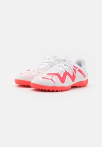 Scarpe da ginnastica bianche con una tomaia testurizzata, accenti rosa brillante, punta arrotondata e suola robusta per una buona trazione. Visibili lacci e logo.