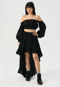 Čierny, ramienka voľne padnúci crop top a maxi sukňa s čipkovou látkou. Sukňa má volánový spodný lem a design s vysokým a nízkym lemom. Nosí sa s čiernymi čižmami.