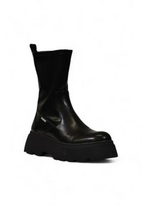 Bottines noires en cuir synthétique avec une semelle épaisse, dotées d'un logo sur le côté et d'un tige large pour un enfilage facile. Fini lisse et brillant.