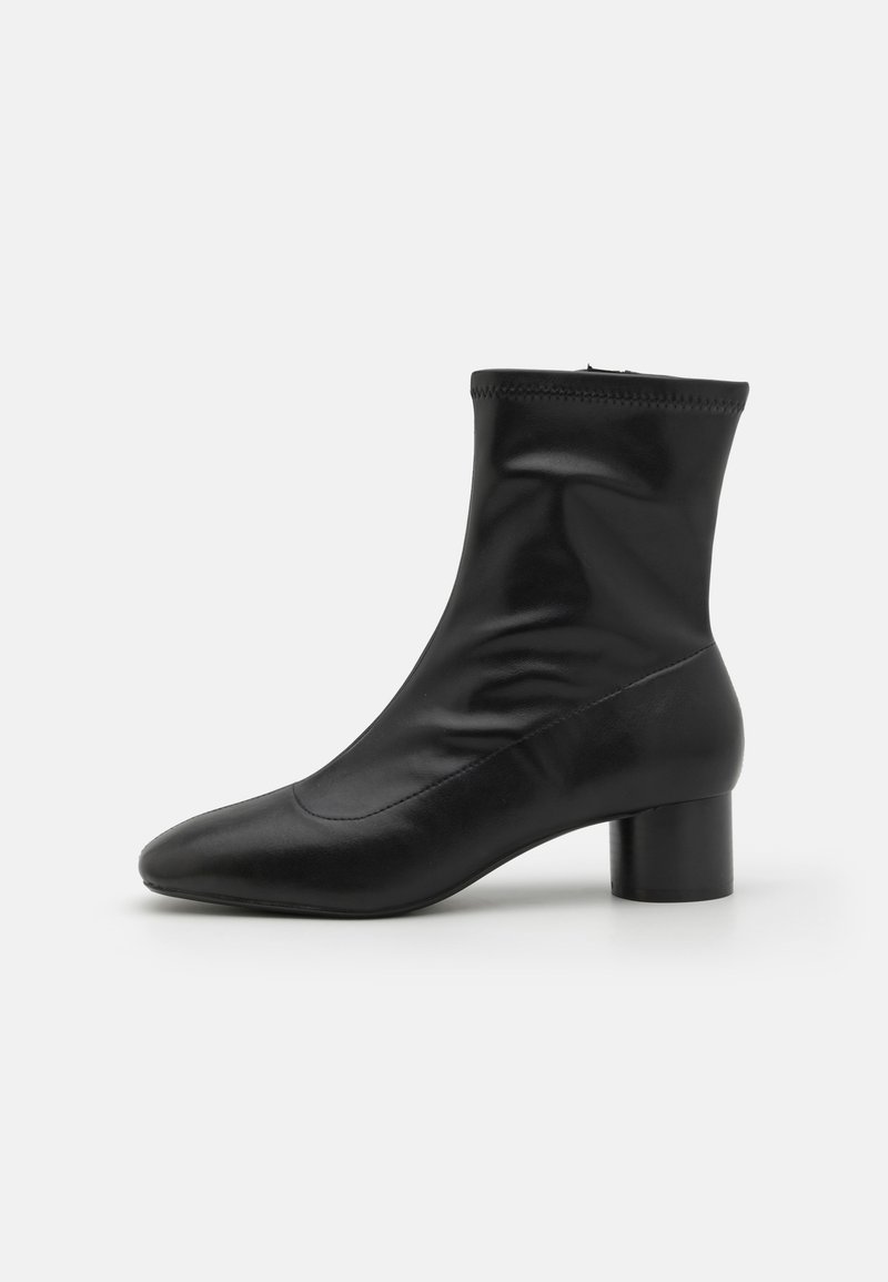 Bottine noire avec une texture en cuir lisse, à bout pointu et talon bloc cylindrique. Présente une silhouette ajustée et une fermeture éclair.