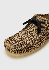 Leopard-print slipper with soft fur texture, black flat laces, and a light-colored sole. Features a rounded toe and stitched detailing.
